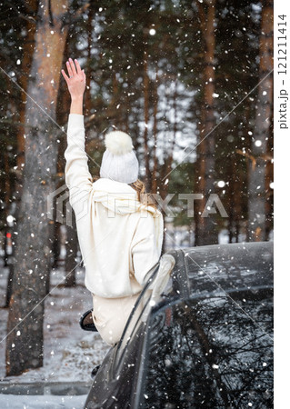 Young woman in woolen white hat have a fun in black car. Winter travel, snow-covered trees in the forest. Snowy weather. Young woman in woolen white hat have a fun in black car. Winter travel, snow-covered trees in the forest. Snowy weather. 121211414