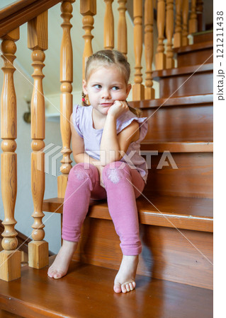 Cute little girl is sitting alone on stairs at home. Dangerous situation at home. Child safety concept. Cute little girl is sitting alone on stairs at home. Dangerous situation at home. Child safety concept. 121211438