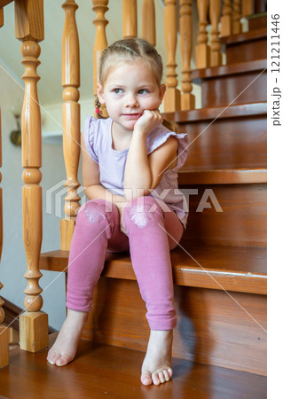 Little girl is sitting alone on stairs at home. Dangerous situation at home. Child safety concept. Little girl is sitting alone on stairs at home. Dangerous situation at home. Child safety concept. 121211446