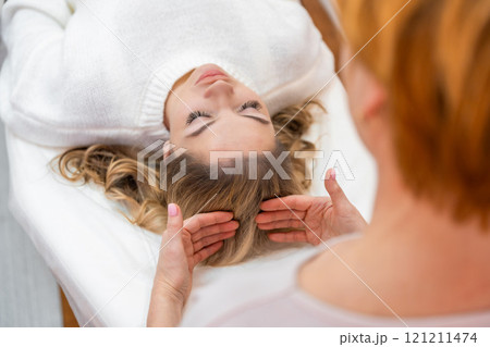 Healer woman performing by lightly touched access bars therapy on young woman head, stimulating positive change thoughts and emotions. Alternative medicine concept 121211474