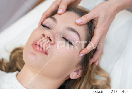 Close up view of healer hands performing by lightly touched access bars therapy on young woman head, stimulating positive change thoughts and emotions. Alternative medicine concept 121211495