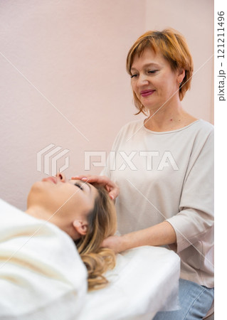 Healer woman performing by lightly touched set of 32 points of access bars on young woman head, stimulating positive change thoughts and emotions. Alternative medicine concept Healer woman performing by lightly touched set of 32 points of access bars on young woman head, stimulating positive change thoughts and emotions. Alternative medicine concept 121211496