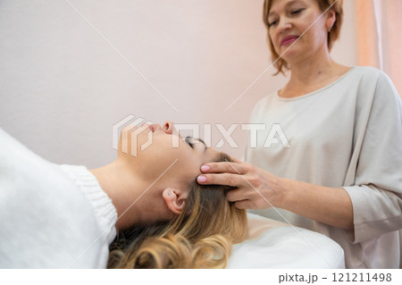 Healer performing by lightly touched set of 32 points of access bars on young woman head, stimulating positive change thoughts and emotions in salon. Alternative medicine concept Healer performing by lightly touched set of 32 points of access bars on young woman head, stimulating positive change thoughts and emotions in salon. Alternative medicine concept 121211498