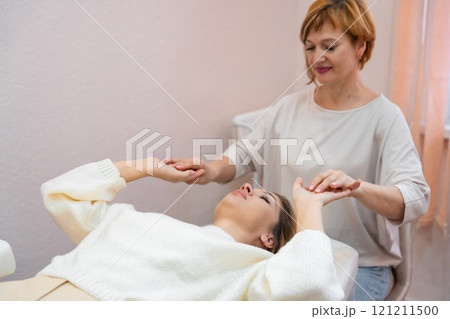 Healer woman launches body energy through hands before access bars therapy with young woman, stimulating positive change thoughts and emotions. Alternative medicine Healer woman launches body energy through hands before access bars therapy with young woman, stimulating positive change thoughts and emotions. Alternative medicine 121211500