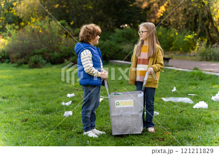 Small children picking up trash together sorting plastic waste into bags in park 121211829