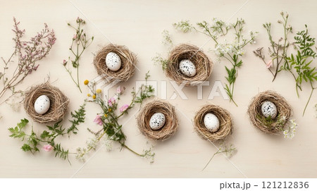Speckled eggs rest in small straw nests, adorned with delicate flowers and greenery, creating a cozy spring ambiance on wood 121212836