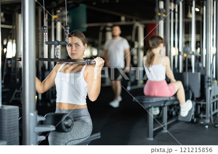 Slender athletic woman work out muscles of hands on cable crossover machine in fitness club 121215856