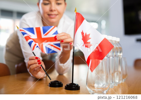 Young woman putting UK and Canada flags on table in office Young woman putting UK and Canada flags on table in office 121216068