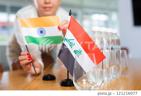 Woman secretary prepares an office for negotiations - she places flags of Iraq and India table Woman secretary prepares an office for negotiations - she places flags of Iraq and India table 121216077