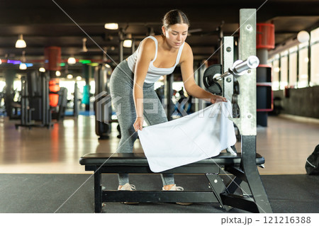 Girl lays white towel on bench, covers simulator for individual training. Girl lays white towel on bench, covers simulator for individual training. 121216388