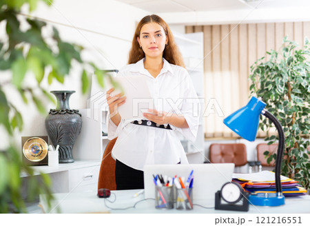 Portrait of a young secretary girl standing in the office near the workplace Portrait of a young secretary girl standing in the office near the workplace 121216551