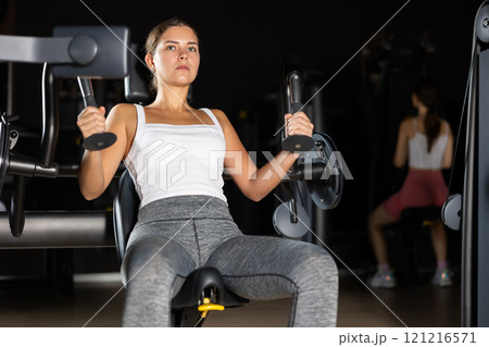 Athletic woman work out muscles of arms and hands on simulator in fitness club 121216571