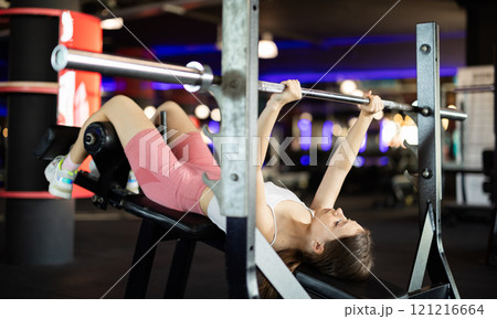 Young woman exercising on barbell machine Young woman exercising on barbell machine 121216664