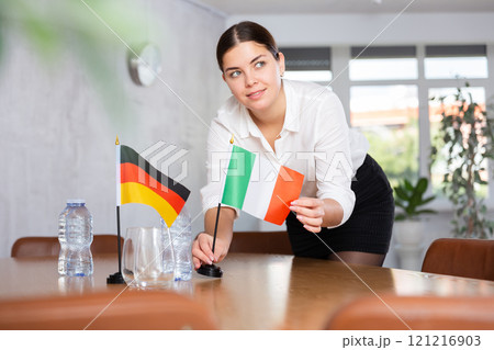 Preparing for business presentation - secretary places flags of Germany and Italy on negotiating table 121216903