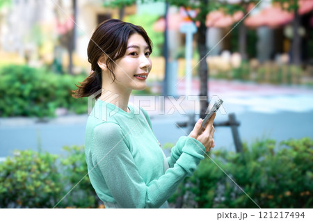 ショッピングしながらスマホを操作するオシャレな若い女性 ショッピングしながらスマホを操作するオシャレな若い女性 121217494