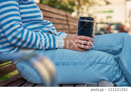 Woman relaxing on bench holding reusable coffee cup in park 121221262