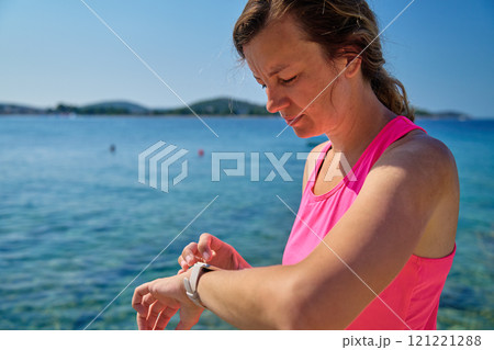Female athlete using fitness watch while running on sunny day Female athlete using fitness watch while running on sunny day 121221288