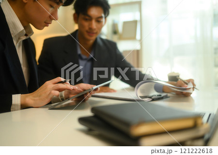 Cropped shot of two businesspeople using a digital tablet and reviewing paperwork at office desk 121222618