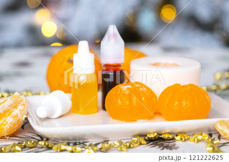 Handmade soap in the form of Orange tangerine  with bottles of dye, flavor, a block of glycerin soap base, silicone mold, on background of Christmas tree with golden light. Soap as gift new year 121222625
