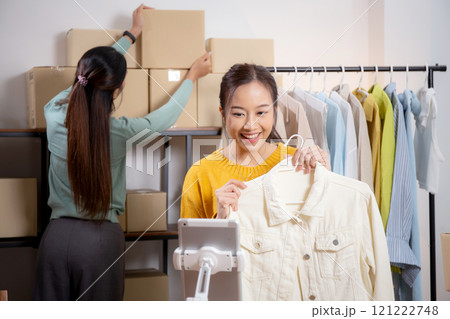Two young asian woman live online clothing store while showing clothing with tablet and laptop. Two young asian woman live online clothing store while showing clothing with tablet and laptop. 121222748