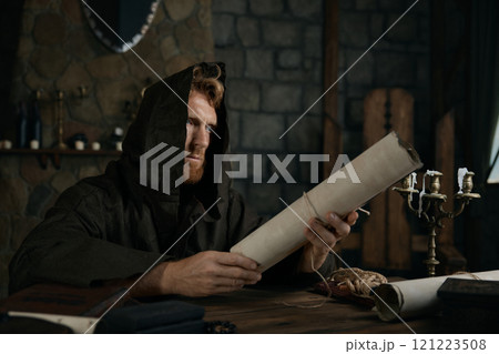 Religious man in hooded cape holding obsolete parchment in hands Religious man in hooded cape holding obsolete parchment in hands 121223508