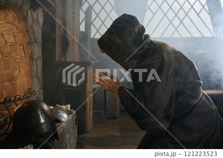 Desperate priest kneeling before church altar in mystical smoke 121223523