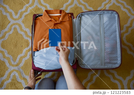 Male hand holding passport over folded clothes in travel suitcase Male hand holding passport over folded clothes in travel suitcase 121223583