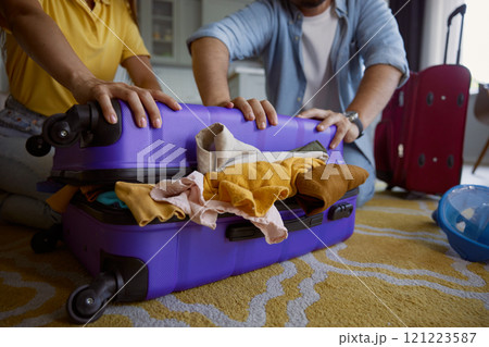 Young loving couple with frowning face trying to close overloaded travel bag Young loving couple with frowning face trying to close overloaded travel bag 121223587