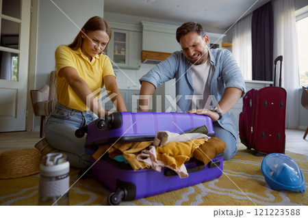 Young loving couple with frowning face trying to close overloaded travel bag Young loving couple with frowning face trying to close overloaded travel bag 121223588
