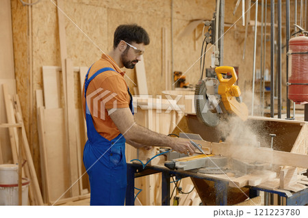 Skilled carpenter sawing wood plank using round circular saw at workbench Skilled carpenter sawing wood plank using round circular saw at workbench 121223780
