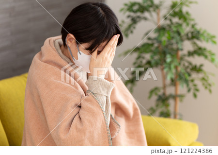 冬の部屋で頭痛に苦しむマスクをつけたミドル〜シニア女性 冬の部屋で頭痛に苦しむマスクをつけたミドル〜シニア女性 121224386