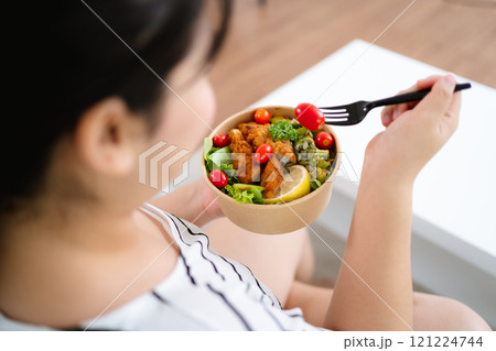 Beautiful Asian woman eating salad, holding a glass bowl and using a fork to pick up a tomato to eat Beautiful Asian woman eating salad, holding a glass bowl and using a fork to pick up a tomato to eat 121224744
