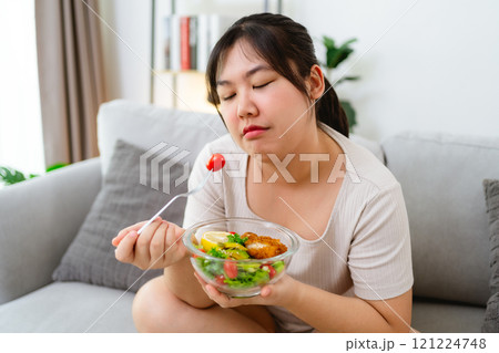 An Asian fat woman feels bad and bored while eating a salad. She doesn't like to eat vegetables. 121224748