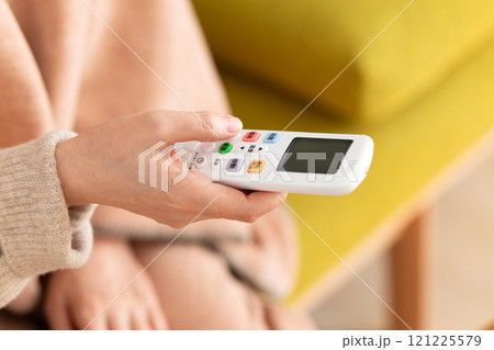 冬のリビングでエアコンのリモコンを持つミドル〜シニア女性 121225579