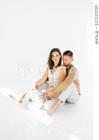 Couple is sitting on the floor with a disco ball in front of them. Scene is playful and fun Couple is sitting on the floor with a disco ball in front of them. Scene is playful and fun 121225595