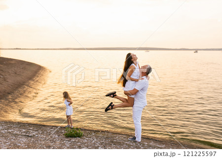 Man and woman are hugging in the water, with child standing nearby. Scene is set on beach, with the ocean in the background Man and woman are hugging in the water, with child standing nearby. Scene is set on beach, with the ocean in the background 121225597