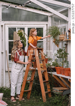Woman mother and two red-haired daughter girls care and plant plants in pots in a greenhouse, doing gardening in the spring for Earth Day. Woman mother and two red-haired daughter girls care and plant plants in pots in a greenhouse, doing gardening in the spring for Earth Day. 121227757