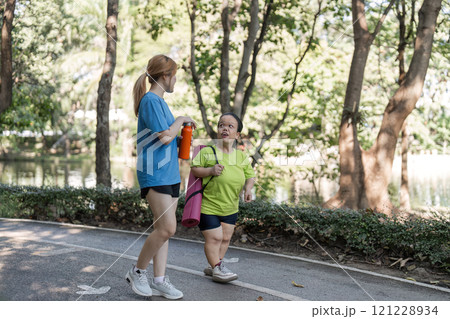 Petite Disabled Woman Exercising in the Park with Supportive Friend on a Sunny Day 121228934