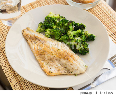 Fried fillet of sea bass with garnish of broccoli on black warm stone plate 121231409