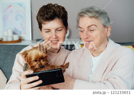 Young woman explaining her senior mother or grandma how to use smartphone for online video call on smartphone. Retired lady discovering mobile technology for calling, texting with natives and friends. 121233651