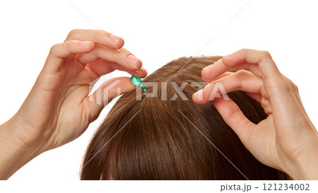 Close-up of woman applying serum capsule on her head skin, hair against white studio background. Treatment, nourishment 121234002