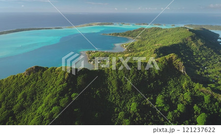 Aerial drone captures the breathtaking beauty of Bora Bora mountains, tropical island in French Polynesia, where lush green vegetation covers volcanic slopes meeting a vibrant turquoise lagoon 121237622