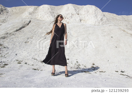 A beautiful girl in a black long dress stands against the background of chalk mountains. A beautiful girl in a black long dress stands against the background of chalk mountains. 121239293