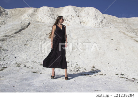 A beautiful girl in a black long dress stands against the background of chalk mountains. A beautiful girl in a black long dress stands against the background of chalk mountains. 121239294