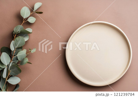 Minimalistic table setting with beige plate and eucalyptus branch on light brown background 121239784