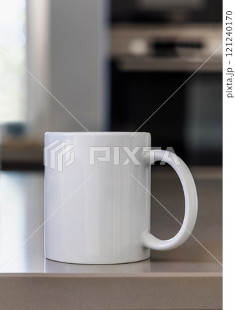 Closeup of  white blank coffee mug on grey kitchen table over blured kitchen interior, mockup 121240170