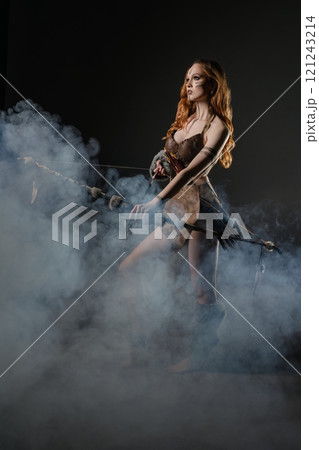 A young woman in a mystical costume walks through smoke-filled darkness 121243214