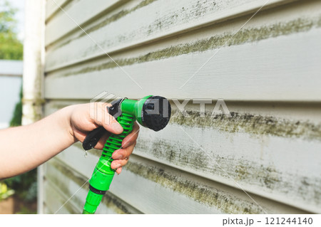 Cleaning algae and mold from vinyl siding of house with brush 121244140