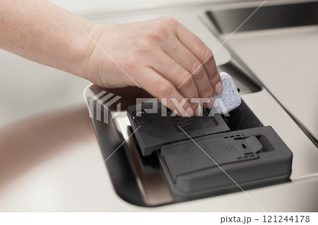 Hand puts soap tablet to dishwashe Hand puts soap tablet to dishwashe 121244178