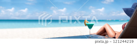 Woman in hat sitting on sunbed with glass of cocktail. Summer vacation on tropical beach. Long banner 121244219